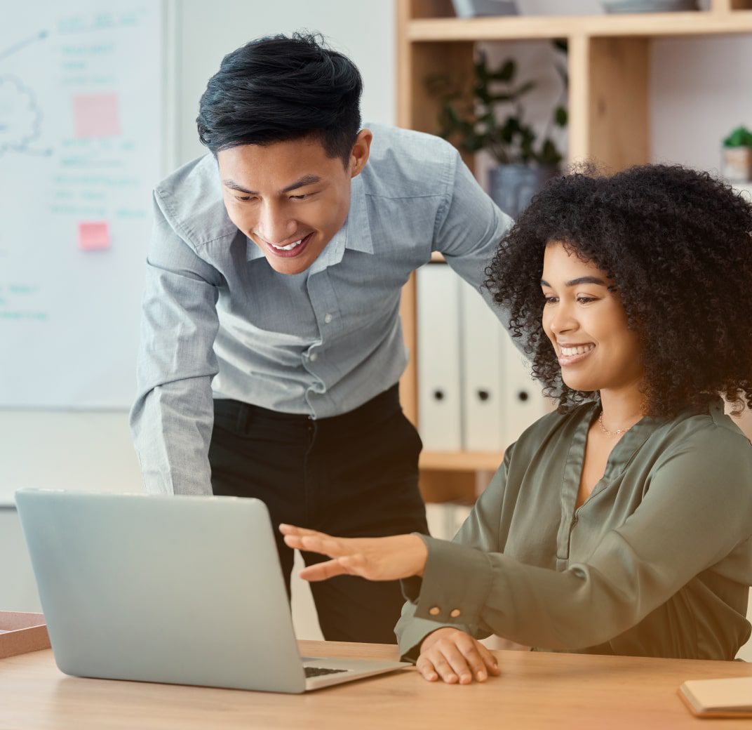 2 marketing professionals smiling and looking at data on a laptop.